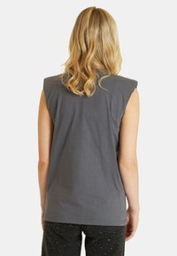 Sleeveless gray cotton top with a relaxed fit. Features a simple design and clean lines, worn with dark pants embellished with small sparkles.