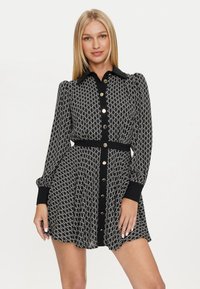 Abito a righe in bianco e nero con collo a camicia, bottonatura frontale e maniche a palloncino. Presenta una vita aderente e una gonna svasata.