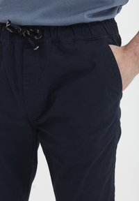 Navy blue elastic-waist pants with a drawstring, featuring side pockets and a smooth, lightweight fabric, tailored for comfort and ease.