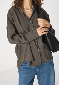 Camicia grigia a maniche lunghe con una vestibilitàampia, apertura frontale con bottoni e texture morbida, abbinata a jeans blu e una borsa nera.