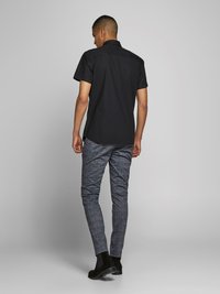 Chemise noire à manches courtes avec un col, associée à un pantalon slim-fit bleu à motif et des bottines noires. Vue arrière sur un fond neutre.