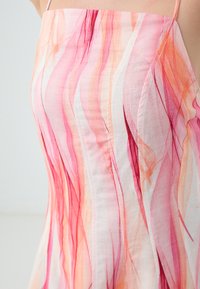 Robe à motifs floraux présentant des rayures fluides roses et orange sur un tissu léger. Bretelles fines et silhouette ajustée.