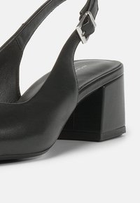 Chaussure noire en cuir à talon bloc avec bride arrière et boucle argent ajustable.