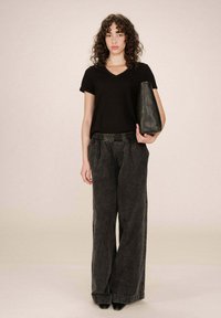 Maglietta nera in cotone a maniche corte, abbinata a pantaloni in denim grigi con vita alta e gamba larga, e una borsa a tracolla in pelle nera elegante.