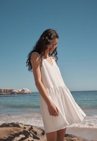 Witte mouwloze jurk met een V-hals, uitlopende rok en geplooide zoom. Zachte stof, lichtgewicht ontwerp en vloeiende silhouet.