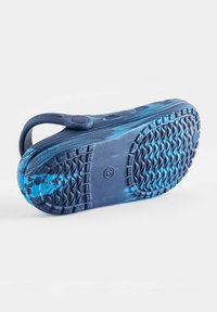 Kék slip-on cipő texturált gumitalppal, sima felsőrésszel, amelyen festett gradiens mintázat található a kék különböző árnyalataiban.
