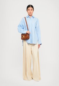 Blue and white striped button-up shirt with long sleeves, paired with cream wide-leg trousers and a brown crossbody bag with gold hardware.