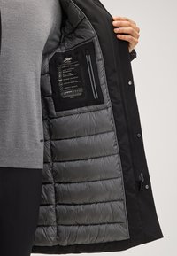 Czarna kurtka z odpinaną szaro izolowaną podszewką. Posiada zamknięte kieszenie, gładką zewnętrzną powłokę oraz instrukcje pielęgnacji na wewnętrznej etykiecie.