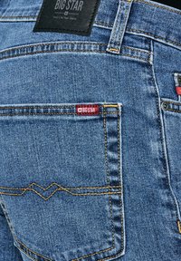 Sinised teksapükste tagatasku kollase õmblusega, punane BIG STAR silt ja must nahast brändiplaaster, millel on kiri "BIG STAR Your Life, Your Jeans."