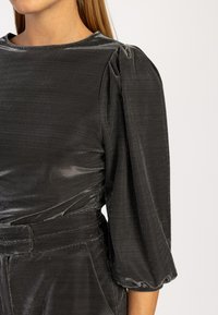 Grijze fluwelen top met een ronde halslijn, gepofte mouwen met elastische manchetten en een gestructureerde afwerking. Inclusief tailleband.
