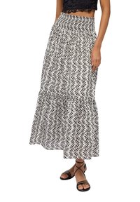 Donna che indossa un crop top nero e una gonna maxi a vita alta con un motivo in bianco e nero, abbinata a sandali piatti neri con fasce.