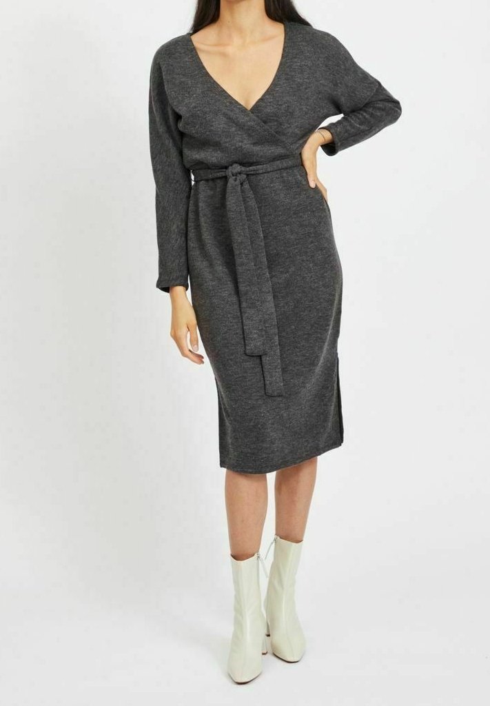 Šedé zavinovací šaty s dlouhými rukávy, výstřihem do V, uvázáním v pase a délkou ke kolenům. Nosené s bílými kotníkovými botami, které mají hladkou strukturu.
