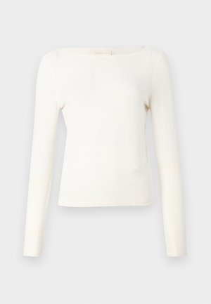 Gara piedurkne blūze gaiškrēm krāsā, ar laivu formas kakla izgriezumu, pieguļošu dizainu un gludu adījuma tekstūru. Minimāls šuvju skaits un bez redzamām rakstainēm.