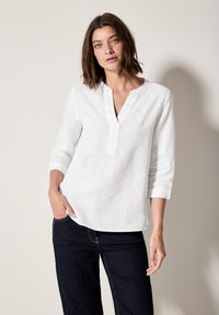 Vit linneskjorta med halvknäppning, tre fjärdedels ärm och avslappnad passform. Kombinerad med en mörk denimjeans. Enkel design och textur.