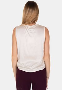 Top senza maniche color crema con vestibilità morbida, texture liscia simile alla seta e scollatura rotonda. Il retro presenta un delicato drappeggio e nessuna chiusura visibile.
