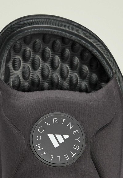 Svart mjukskalskepp med en strukturerad, mönstrad insida och en cirkulär logotyp med namnet "McCartney" och en design med tre ränder.