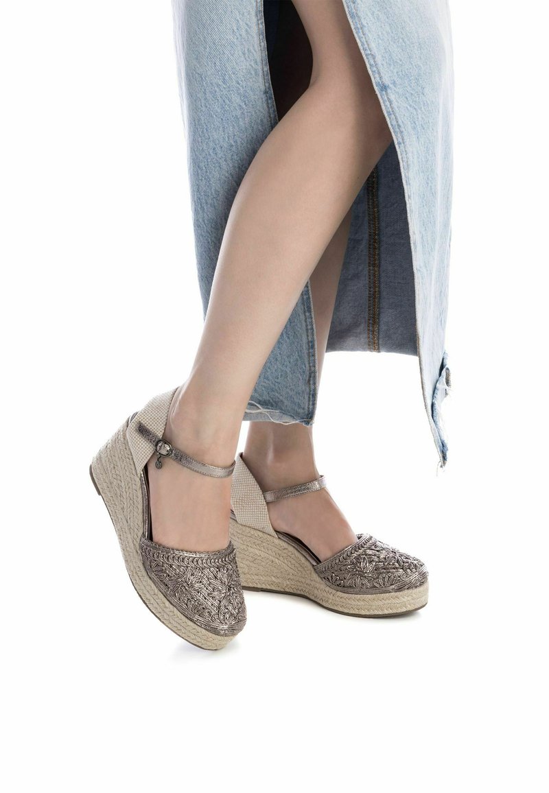 Espadrilles de cuña con un acabado metálico, bordados intrincados y una correa en el tobillo. Fabricadas con tejido texturizado y suela de fibra natural.