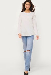 Langærmet lysegrå top kombineret med lyseblå ripped jeans; jeansene har slidte områder ved knæene, båret med sorte høje hæle.