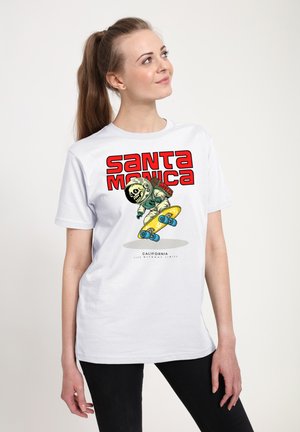 Hvid bomulds t-shirt med et grafisk design, der viser et tegneserie-skelet i rumeventyrdragt, der står på et gult skateboard, tekst "Santa Monica" i rød.