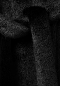 Tejido de piel sintética negra, con una textura suave y densa y longitudes de pelo variadas. El diseño de bucle crea profundidad e interés visual.