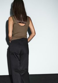 Brown tank top with a scoop back, paired with high-waisted black pants featuring two back pockets and visible stitching details.