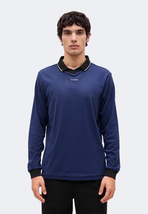 Un mannequin masculin se tient devant un fond clair, vêtu d’un polo bleu marine à manches longues, avec un col et des poignets noirs.