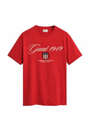 T-shirt en coton rouge avec le texte "Gant 1949" en écriture blanche, accompagné d'un graphique de blason et de "American Sportswear Connecticut" en dessous.