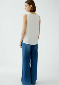 Haut sans manches blanc associé à un jean en denim bleu à jambes larges. Le haut présente un tissu lisse et un col arrondi.