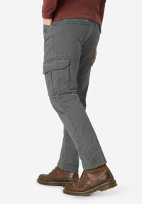 Gray cargo pants with side pockets, tapered legs, and visible stitching. Worn with brown lace-up boots and a maroon long-sleeve top.