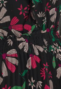 Schwarzer Stoff mit floralen Mustern, die rosa, weiße und grüne Blumen und Blätter zeigen, elastischer Rüscheldetail in der Mitte.