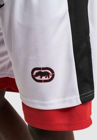 Witte mesh shorts met rode details, voorzien van een zwarte zijpaneel. Opmerkelijk geborduurd logo met een neushoorn binnen een ovaal.