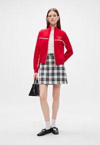 Cazadora roja con cremallera y detalles blancos, camiseta blanca, falda de cuadros en blanco y negro, bolso negro y zapatos negros con tiras.