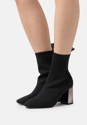 Bottines noires style chaussette avec un bout pointu et un talon chunky translucide. Fabriquées en tissu extensible au toucher lisse.