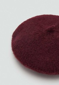 Bordový vlnený baret s jemnou textúrou, guľatým tvarom a malým uzlíkom na vrchu. Ľahký a pružný dizajn.