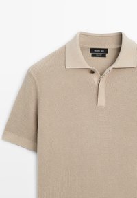 Polo beige en maille 100 % coton, avec un col classique, des manches courtes et une patte de boutonnage à un seul bouton.