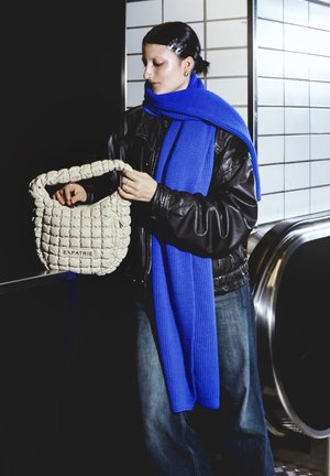 White, quilted handbag with a chunky handle and "EXPATRIE" label; worn with a blue knit scarf and black leather jacket.