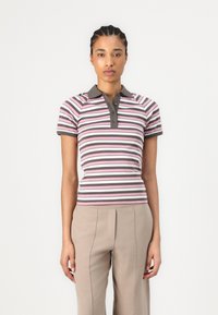Randig polo skjorta i rosa, mauve och brunt med mörk krage och knappar, kombinerad med ljusbeiga byxor. Korta ärmar och figurnära design.
