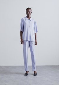 Light purple, short-sleeve button-up shirt paired with matching straight-leg trousers, both made of a smooth, lightweight fabric.