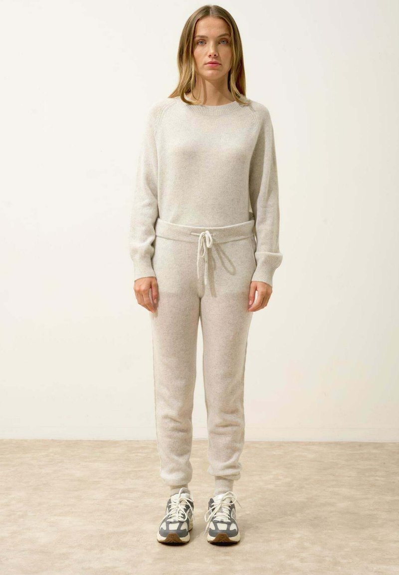 Ljust grå garntröja och matchande joggers med dragsko i midjan, ribbade mudd och mjukt, texturerat tyg. Avslappnade sportiga sneakers.