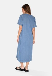 Denim haljina svijetloplave boje, kratkih rukava, s opuštenim krojem i rubom do gležnjeva. Ima vidljive šavove i bočne džepove.