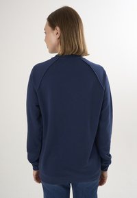 Felpa blu navy con maniche raglan, tessuto morbido, polsini e orlo a coste, e un classico scollo rotondo. Vista dalla parte posteriore.