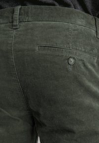 Dunkelgrüne Cordhosen aus strukturiertem Rippstoff, mit einer Gesäßtasche mit Knopfverschluß und einem glatten Bund.