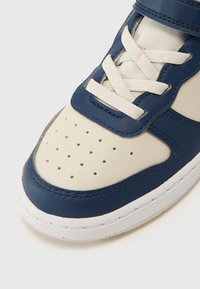 Baskets en cuir bleu et crème avec bout perforé, lacets plats crème et languette rembourrée, dotées d'une semelle en caoutchouc blanche et de détails de couture.