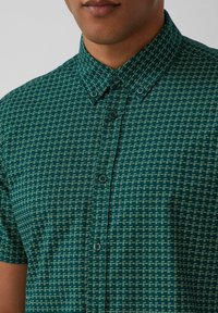 Groene korte mouw shirt met een geometrisch patroon in lichtere tinten. Kraag met knopen in dezelfde kleur. Glad stoffen textuur.