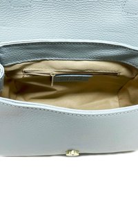 Interior de un bolso de cuero azul claro con un bolsillo con cremallera. Forro de tela suave y texturizada en beige. Incluye un cierre metálico a presión.