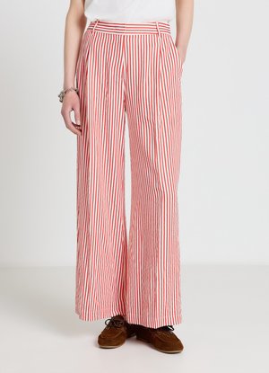 Weit geschnittene Hose mit vertikalen roten und weißen Streifen, kombiniert mit braunen Schnürschuhen und einem weißen Oberteil.