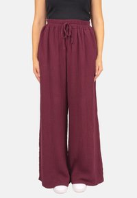 Burgunderfarbene weite Hosen aus strukturiertem Stoff mit elastischem Bund und Kordelzug. Kombiniert mit weißen Schuhen und einem schwarzen Oberteil.