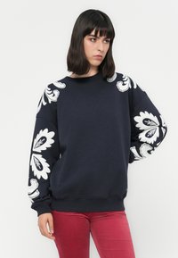 Sudadera azul marina con patrones florales blancos en las mangas. Presenta un cuello redondo y un ajuste relajado, confeccionada en suave tejido de algodón.