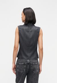 Tamsiai plautas džinsinis liemenė be rankovių, aptemptos formos, su smailiomis apykaklėmis ir subtilia vertikali tekstūra; derinama su aukšto juosmens juodomis džinsais.