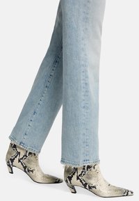 Botki za kostkę w wzór węża z szpiczastym noskiem i blokowym obcasem, wykonane z gładkiego materiału. Noszone z jasnoniebieskimi dżinsami z postrzępionym dołem.